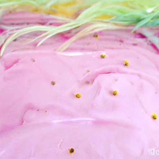 Close-up of a field of wrinkly pink frosting studded with tiny gold balls. In the background is yellow-green hair.