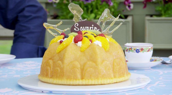 A yellow bundt cake topped with sliced oranges, strawberries, kiwi, and blueberries on top of a thin layer of cream.