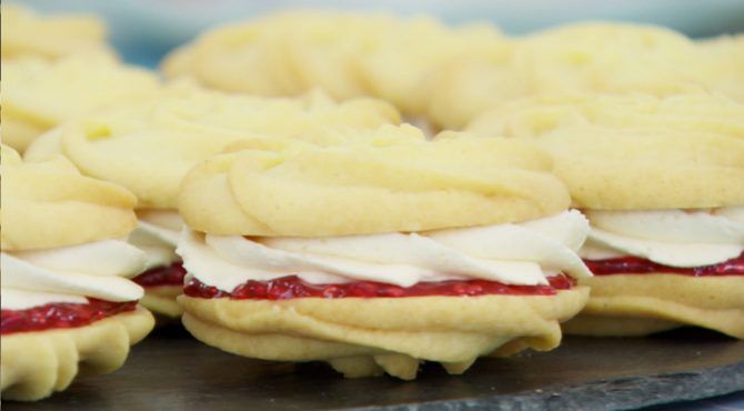 Pale sandwich cookies with a swirl of white frosting and a thin layer of raspberry jam inside.