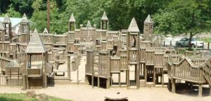 A sprawling playground made of weathered wood, a giant complex with lots of stairs and levels and bridges, dominated by turrets and slatted railings.