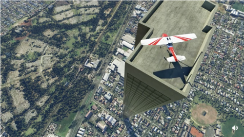 A small two-person plane on the roof of a 212-story building surrounded by a 1-story suburb. View looks steeply down toward the ground. The top of the building seems to be only about an eighth of a city block in size