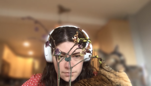 Janelle with an orchid in front of her face and a cat beside her. The cat’s head, and any part of the orchid that does not overlap her head, is blurred.